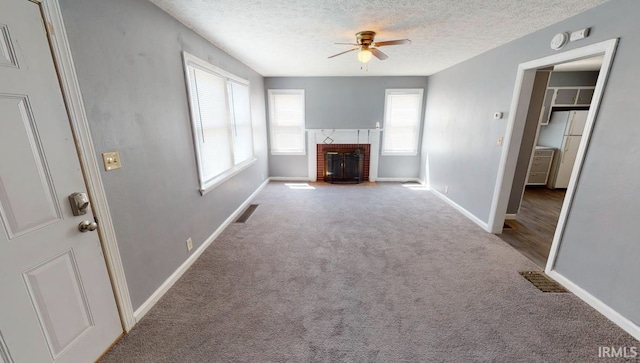 unfurnished living room featuring ceiling fan, carpet flooring, a textured ceiling, and a fireplace