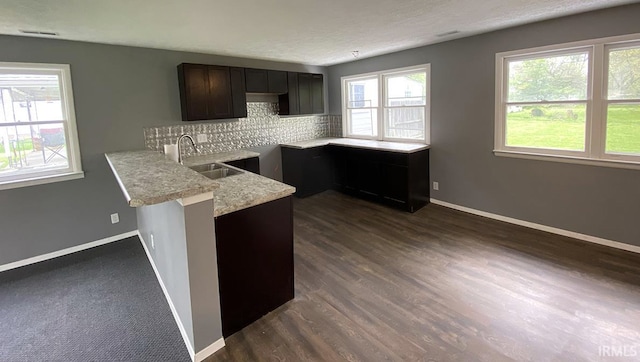 kitchen with dark wood-type flooring, kitchen peninsula, backsplash, sink, and dark brown cabinetry