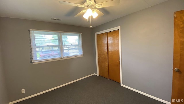 unfurnished bedroom featuring dark colored carpet, a closet, and ceiling fan