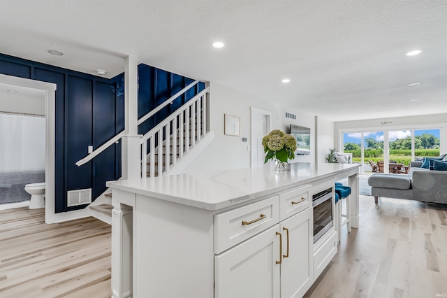 kitchen with stainless steel microwave, light hardwood / wood-style flooring, white cabinets, light stone counters, and a textured ceiling