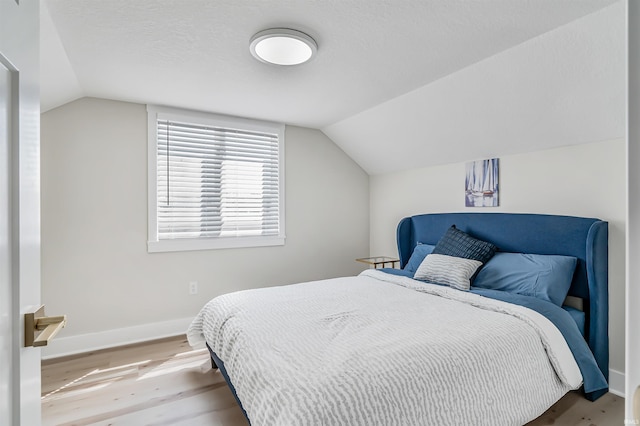 bedroom featuring lofted ceiling, a textured ceiling, and light wood-type flooring