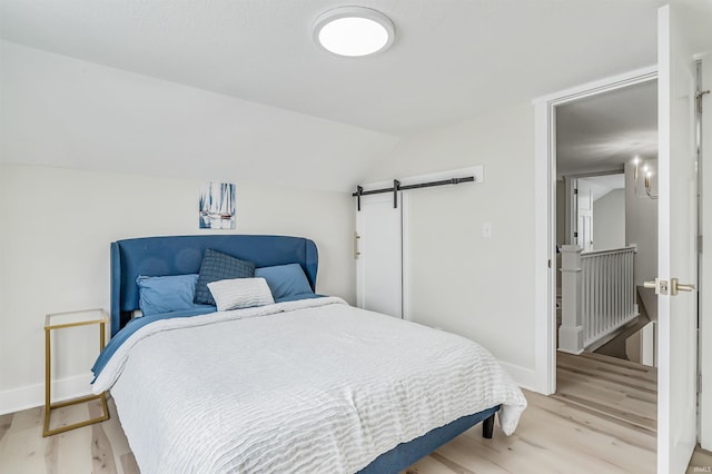 bedroom with light hardwood / wood-style floors, vaulted ceiling, and a barn door