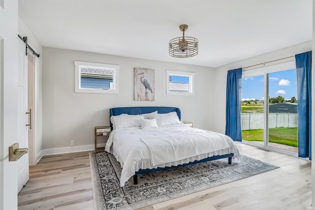 bedroom with light hardwood / wood-style floors, a barn door, and access to exterior