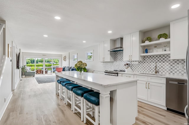 kitchen featuring appliances with stainless steel finishes, wall chimney exhaust hood, white cabinets, and sink