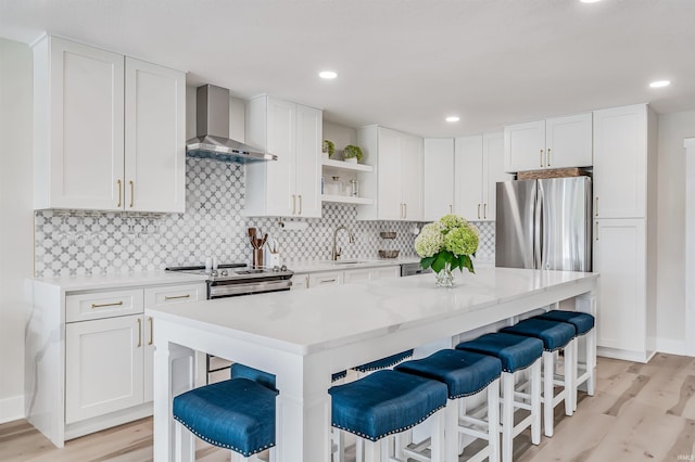 kitchen with appliances with stainless steel finishes, wall chimney exhaust hood, a kitchen island, and a breakfast bar area