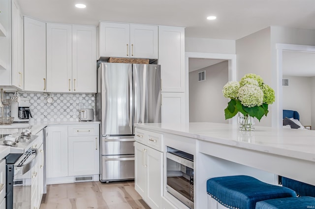 kitchen featuring a breakfast bar area, stainless steel appliances, backsplash, light stone countertops, and light hardwood / wood-style floors