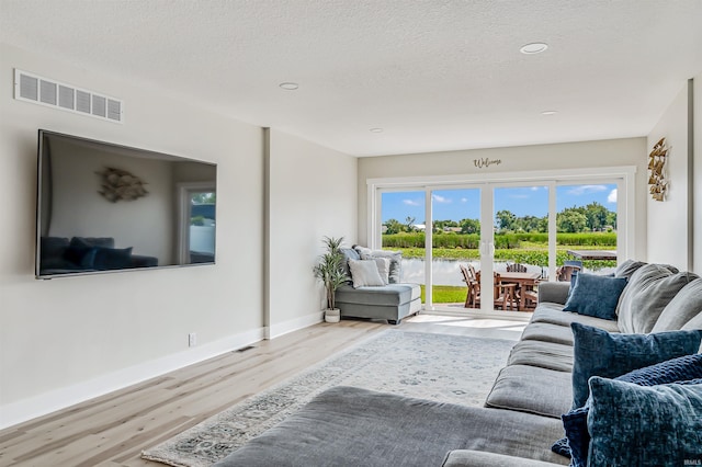 living room with light hardwood / wood-style floors, a textured ceiling, and a water view