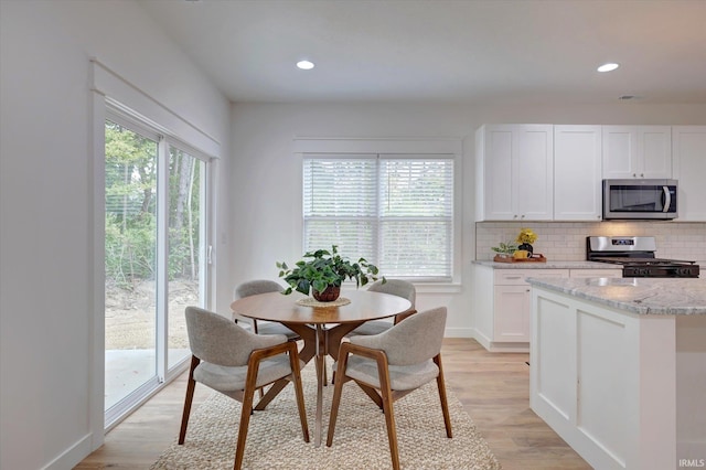 kitchen with white cabinets, decorative backsplash, appliances with stainless steel finishes, light hardwood / wood-style flooring, and light stone counters