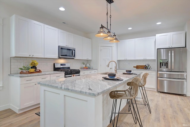 kitchen with a kitchen island with sink, light hardwood / wood-style flooring, stainless steel appliances, light stone countertops, and white cabinetry