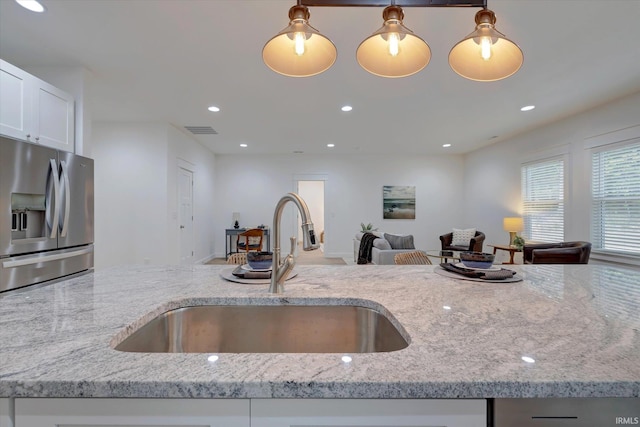 kitchen featuring sink, light stone countertops, stainless steel fridge with ice dispenser, and decorative light fixtures