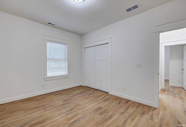 unfurnished bedroom featuring a closet, a textured ceiling, and light wood-type flooring