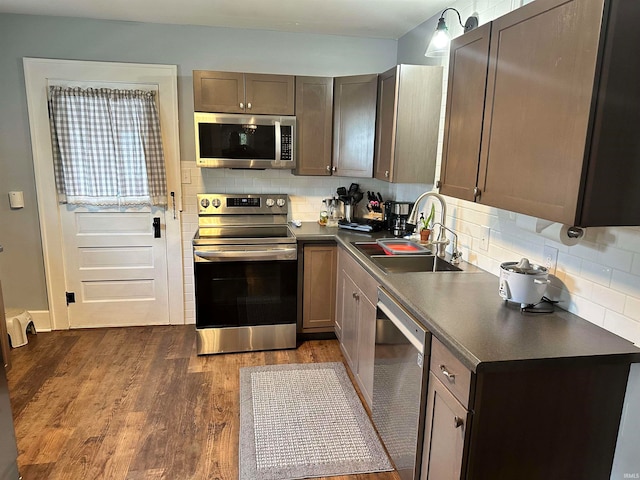 kitchen with appliances with stainless steel finishes, sink, backsplash, and dark hardwood / wood-style flooring