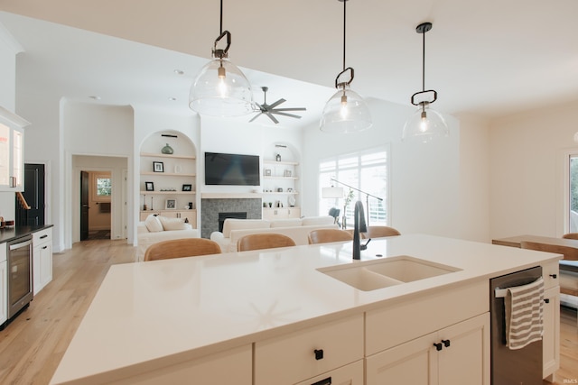 kitchen featuring wine cooler, a kitchen island with sink, pendant lighting, light hardwood / wood-style floors, and sink