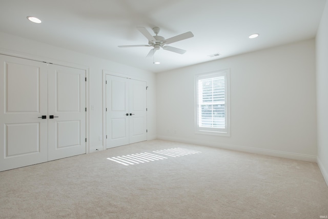 unfurnished bedroom with two closets, light colored carpet, and ceiling fan