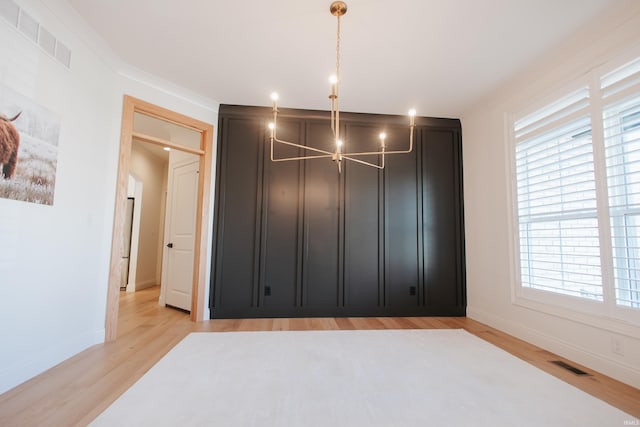 unfurnished bedroom featuring light hardwood / wood-style floors, crown molding, and an inviting chandelier