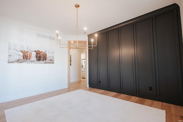 unfurnished bedroom with light hardwood / wood-style floors, a chandelier, and stainless steel refrigerator with ice dispenser