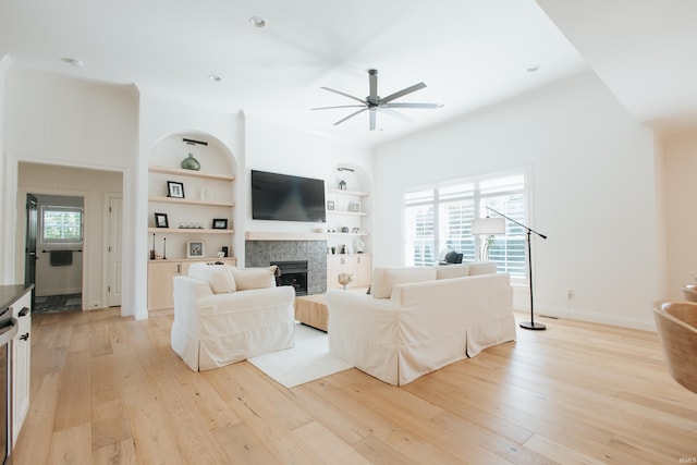 living room with light wood-type flooring, built in features, plenty of natural light, and a tile fireplace