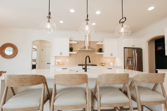 kitchen featuring wall chimney exhaust hood, stainless steel fridge with ice dispenser, pendant lighting, and white cabinets