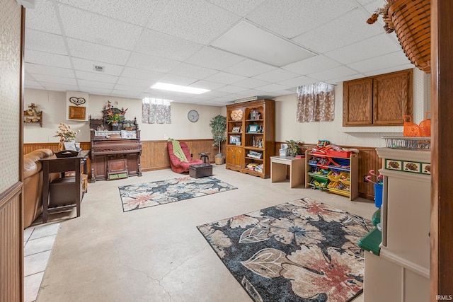 rec room with a paneled ceiling and wooden walls