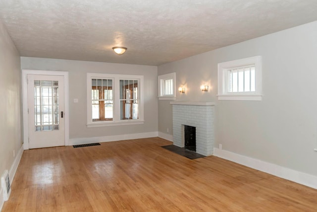 unfurnished living room with light hardwood / wood-style flooring, a textured ceiling, plenty of natural light, and a brick fireplace