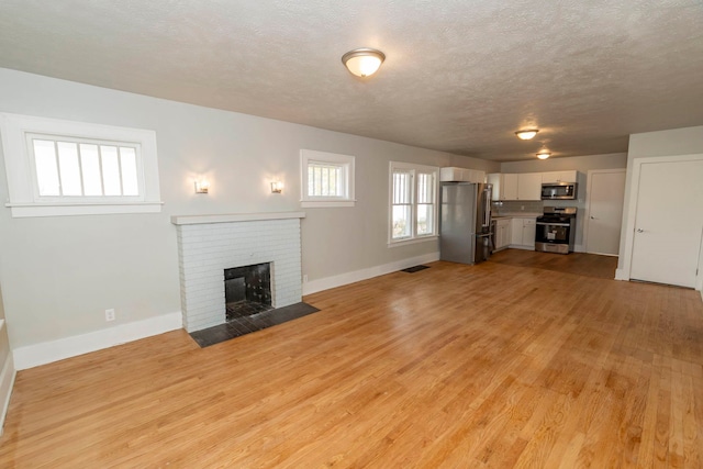 unfurnished living room with a textured ceiling, light wood-type flooring, and a brick fireplace