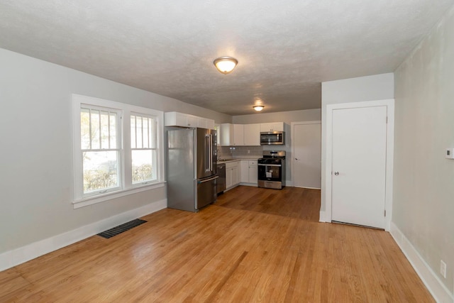 kitchen with appliances with stainless steel finishes, a textured ceiling, white cabinetry, and light hardwood / wood-style floors