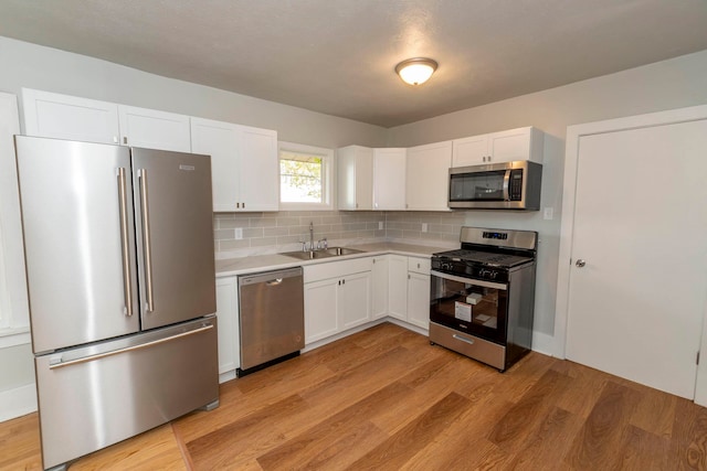 kitchen with sink, backsplash, white cabinetry, light hardwood / wood-style floors, and stainless steel appliances