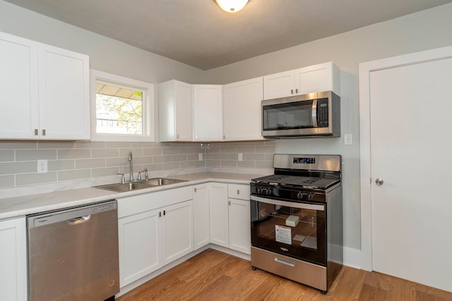 kitchen with appliances with stainless steel finishes, sink, light wood-type flooring, and white cabinets