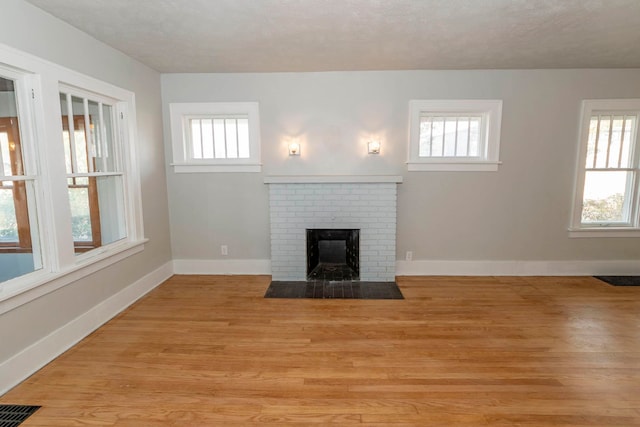 unfurnished living room featuring light wood-type flooring, a textured ceiling, plenty of natural light, and a fireplace