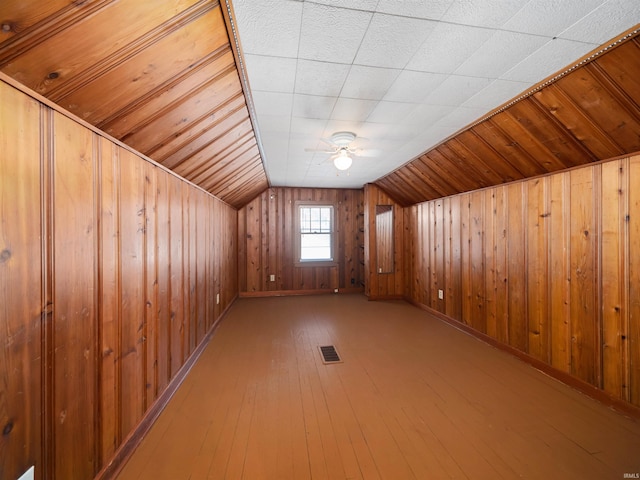 bonus room with lofted ceiling, hardwood / wood-style flooring, wooden walls, and ceiling fan