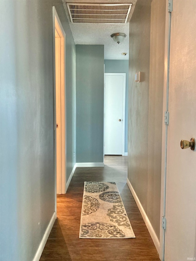 corridor with a textured ceiling and dark hardwood / wood-style floors