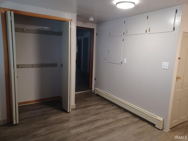 unfurnished bedroom with a closet, wood-type flooring, and a baseboard heating unit