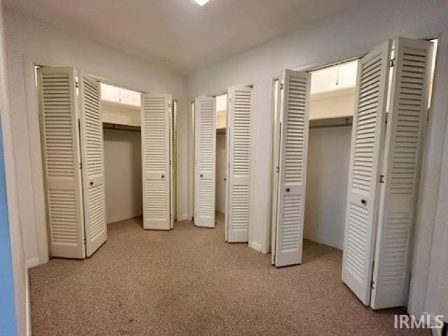 unfurnished bedroom featuring multiple closets and light colored carpet