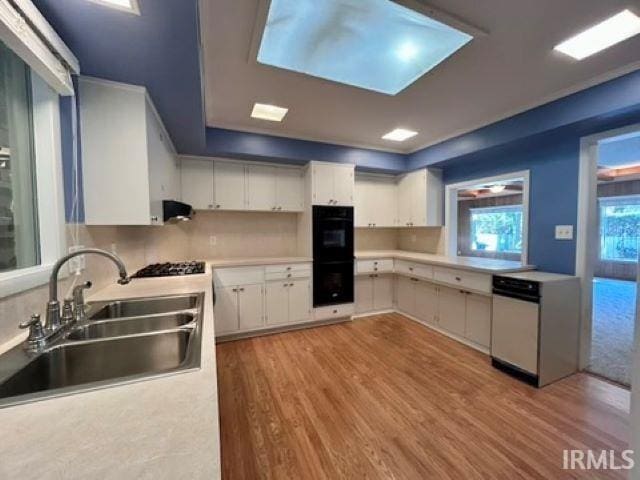 kitchen featuring stainless steel dishwasher, white cabinets, sink, and light wood-type flooring