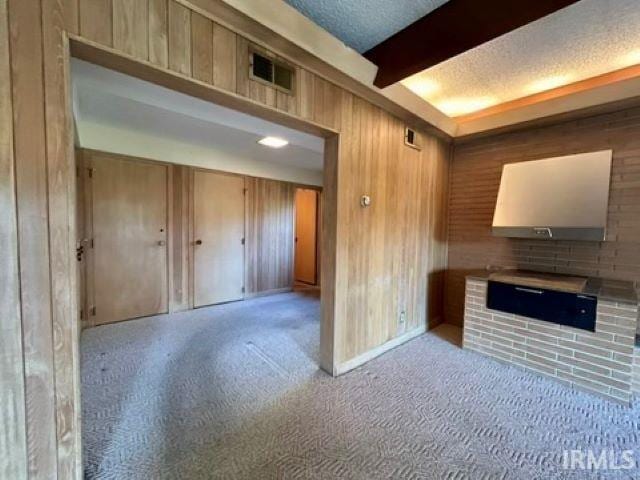 unfurnished living room featuring beam ceiling, light carpet, and wood walls