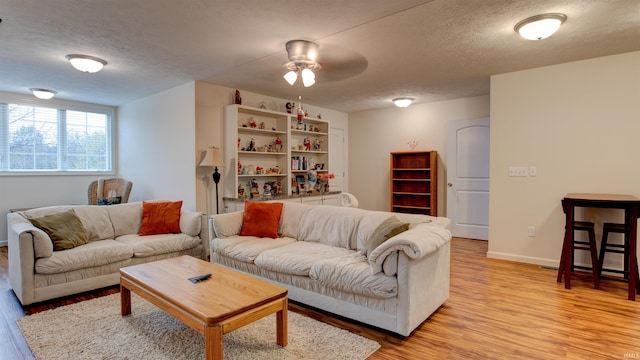 living room with a textured ceiling, light wood-type flooring, and ceiling fan