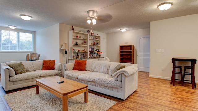 living room featuring a textured ceiling, baseboards, light wood-type flooring, and a ceiling fan