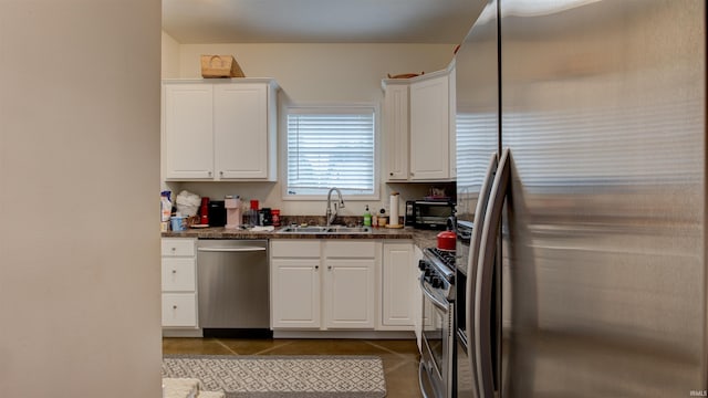 kitchen with dark tile patterned flooring, sink, stainless steel appliances, white cabinets, and dark stone countertops