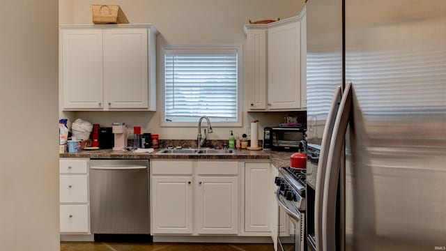 kitchen featuring dark countertops, appliances with stainless steel finishes, white cabinetry, and a sink