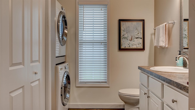 bathroom with vanity, stacked washer / dryer, plenty of natural light, and toilet