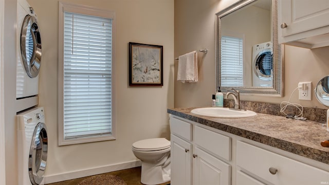bathroom with plenty of natural light, baseboards, toilet, vanity, and stacked washer and clothes dryer