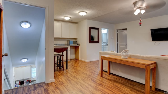 kitchen with a breakfast bar area, ceiling fan, stainless steel microwave, white cabinets, and light wood-type flooring