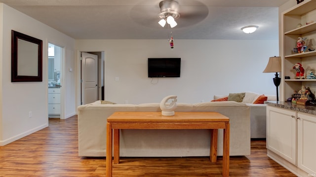 living area with baseboards, ceiling fan, and wood finished floors