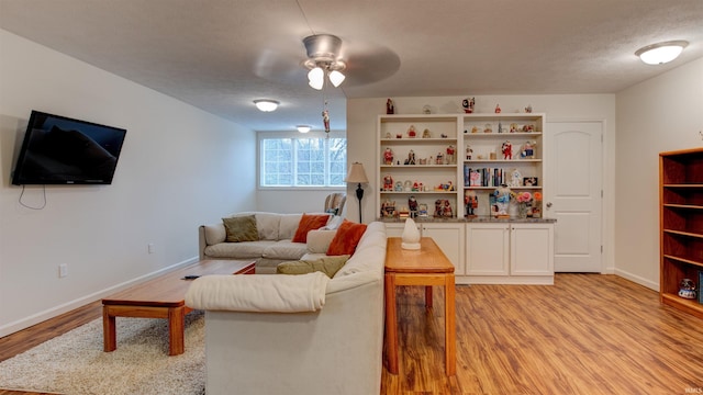 living area featuring a ceiling fan, baseboards, light wood finished floors, and a textured ceiling