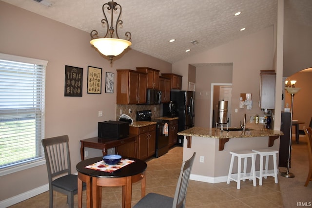 kitchen featuring a breakfast bar, lofted ceiling, light tile patterned flooring, a sink, and black appliances