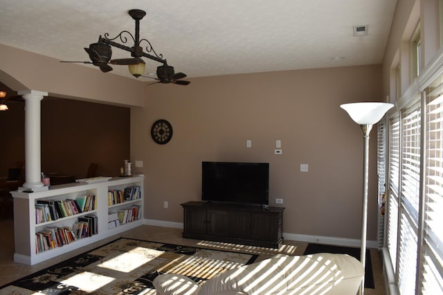 tiled living area with baseboards, a textured ceiling, decorative columns, and a ceiling fan