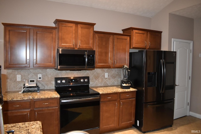 kitchen with black appliances, light stone counters, backsplash, and brown cabinets