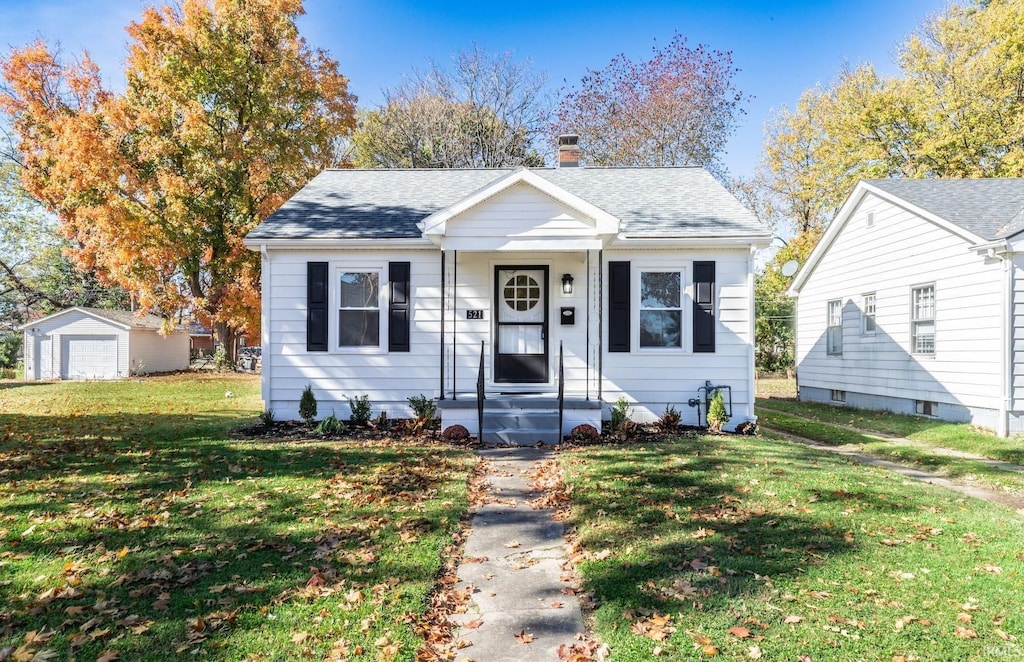 bungalow with a front yard, a garage, and an outbuilding