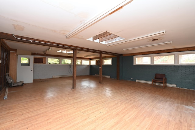 basement with a baseboard radiator, brick wall, and light hardwood / wood-style flooring