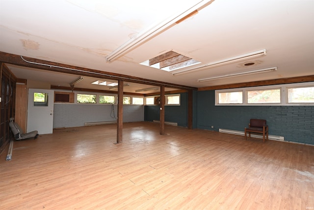 basement with baseboard heating, brick wall, and light hardwood / wood-style floors